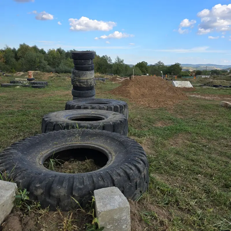 Trei anvelope uriase culcate in sir, un turn de anvelope si o movila de pamant in spate