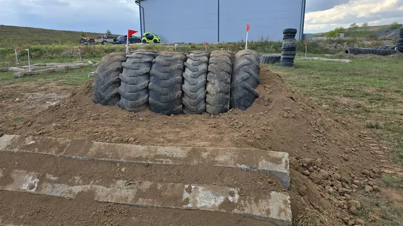 Sase anvelope de tractor puse in picioare intr-o rampa de pamant, cu doua trepte de beton in fata